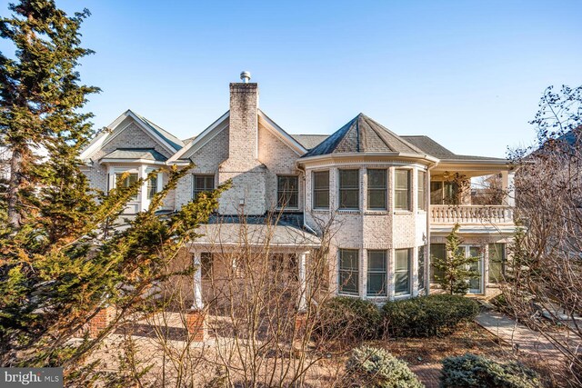 view of front facade with a chimney, brick siding, and a balcony