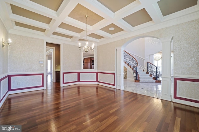 spare room featuring a notable chandelier, wood finished floors, stairs, beamed ceiling, and decorative columns