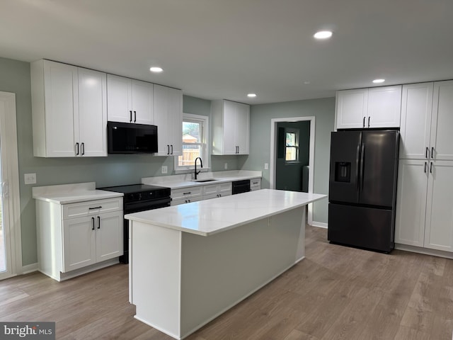 kitchen with black appliances, a center island, white cabinets, and light hardwood / wood-style flooring