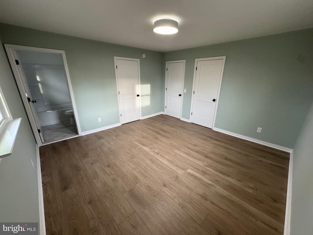 unfurnished bedroom with hardwood / wood-style flooring, ensuite bathroom, and multiple closets