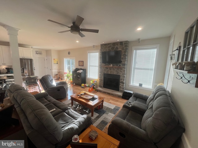 living room featuring a stone fireplace, ceiling fan, and light hardwood / wood-style floors