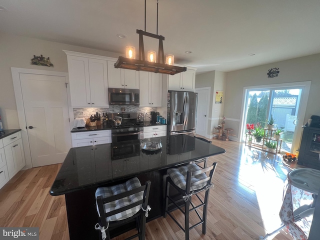 kitchen featuring backsplash, stainless steel appliances, decorative light fixtures, white cabinets, and a kitchen island