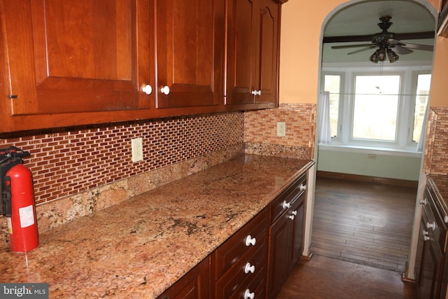 kitchen with tasteful backsplash, light stone counters, dark hardwood / wood-style flooring, and ceiling fan