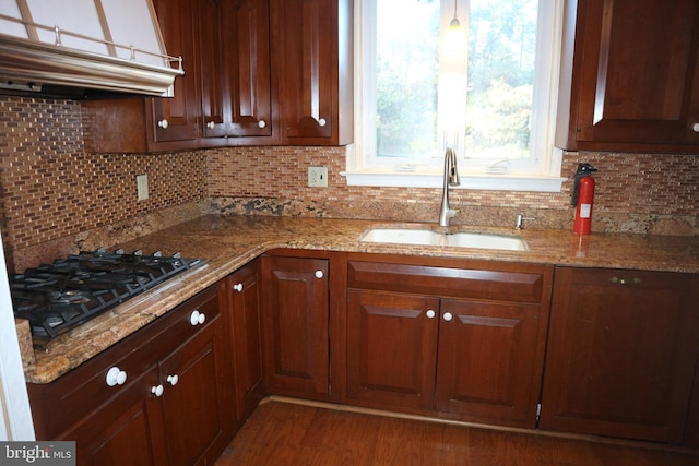 kitchen featuring dark wood-type flooring, black gas stovetop, sink, decorative backsplash, and light stone countertops