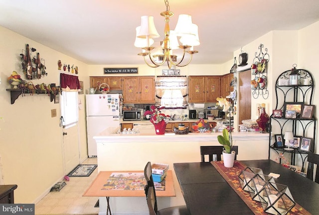 kitchen featuring white fridge, kitchen peninsula, hanging light fixtures, and an inviting chandelier