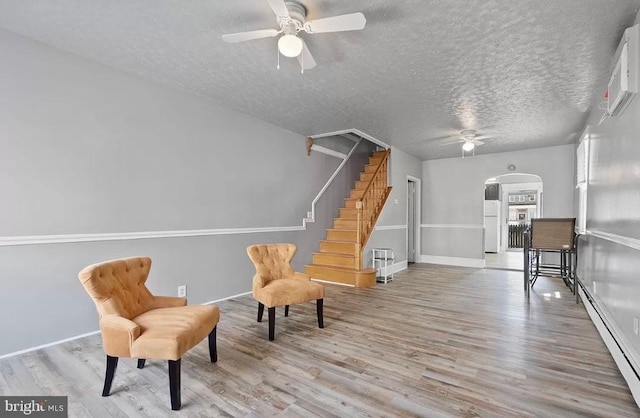 living area featuring baseboard heating, ceiling fan, a textured ceiling, and light wood-type flooring