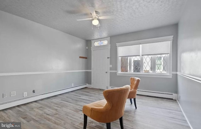 sitting room with baseboard heating, ceiling fan, a textured ceiling, and light wood-type flooring