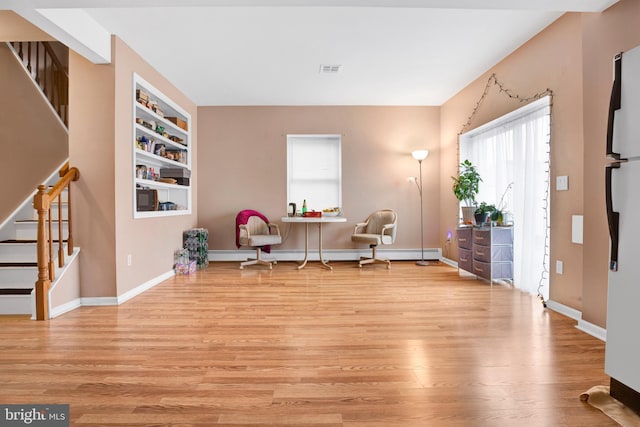 living area with built in shelves, light hardwood / wood-style flooring, and a baseboard radiator