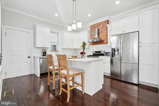 kitchen featuring hanging light fixtures, wall chimney exhaust hood, appliances with stainless steel finishes, tasteful backsplash, and white cabinetry