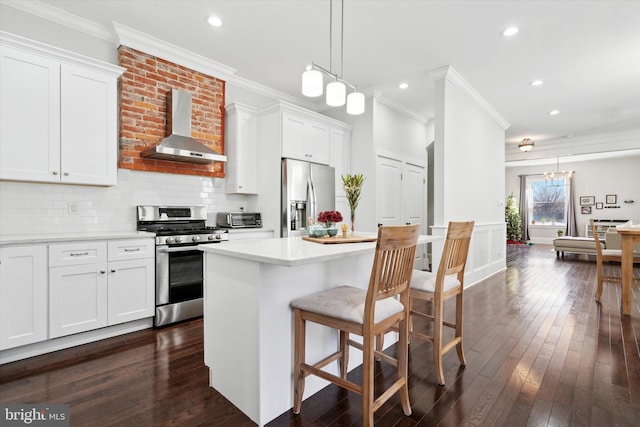 kitchen with white cabinetry, wall chimney exhaust hood, decorative light fixtures, and appliances with stainless steel finishes