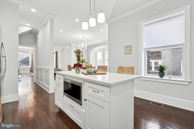 kitchen featuring crown molding, stainless steel microwave, white cabinets, and hanging light fixtures