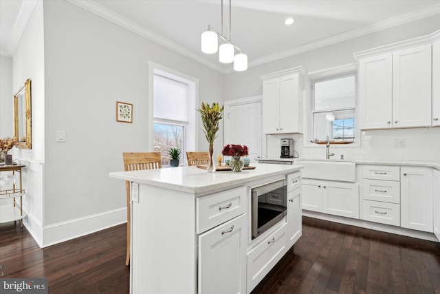 kitchen with decorative backsplash, sink, white cabinets, a center island, and stainless steel microwave