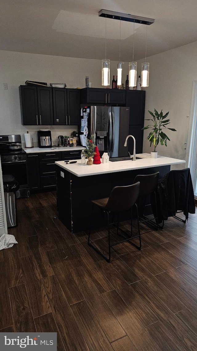 kitchen featuring a breakfast bar, stainless steel refrigerator with ice dispenser, decorative light fixtures, and an island with sink