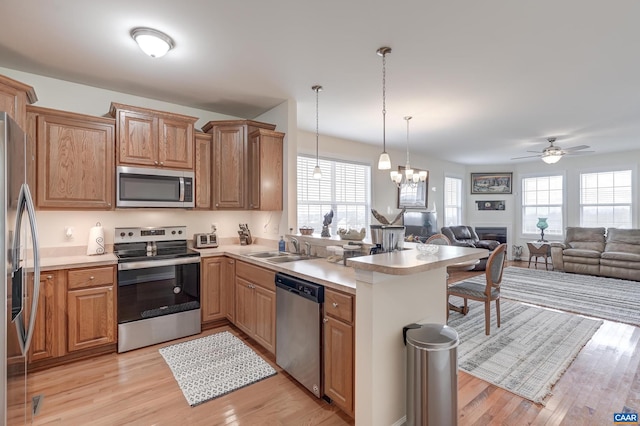 kitchen featuring kitchen peninsula, appliances with stainless steel finishes, ceiling fan with notable chandelier, sink, and hanging light fixtures