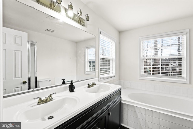 bathroom with vanity, toilet, and tiled tub