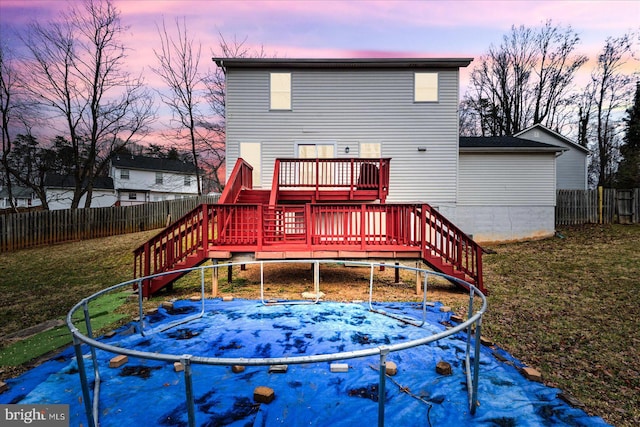 back house at dusk with a trampoline, a yard, and a wooden deck