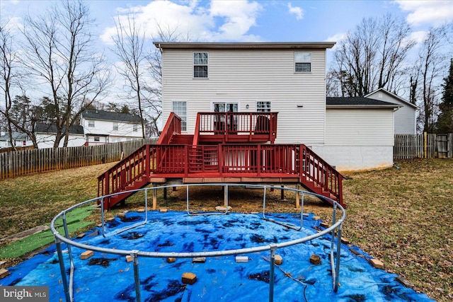 back of property featuring a wooden deck, a yard, and a trampoline