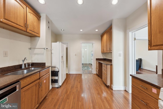 kitchen with sink, stainless steel dishwasher, white refrigerator with ice dispenser, dark stone countertops, and light wood-type flooring