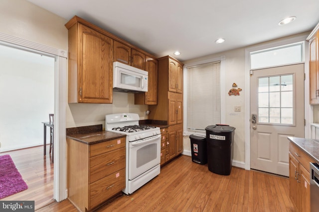 kitchen with light hardwood / wood-style flooring, dark stone counters, and white appliances