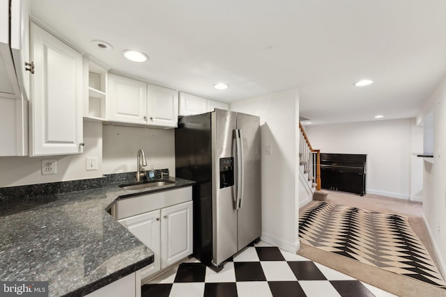 kitchen with white cabinets, stainless steel fridge, dark stone countertops, and sink