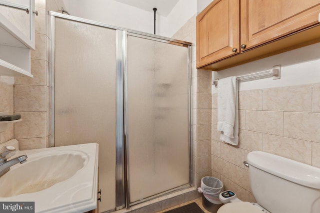 bathroom featuring sink, a shower with door, tile walls, and toilet