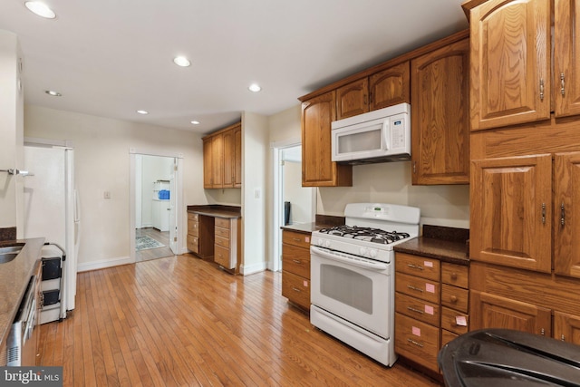 kitchen with dark stone counters, white appliances, and light wood-type flooring