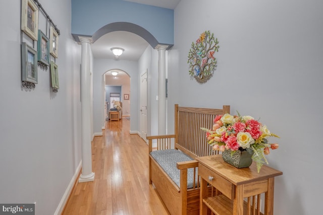 hallway featuring light wood-type flooring and decorative columns