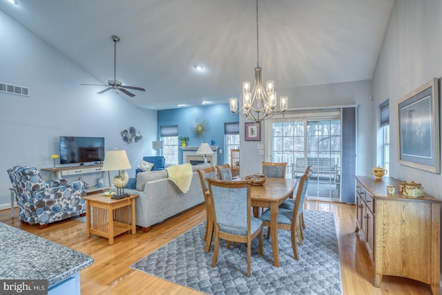 dining space with ceiling fan with notable chandelier, light hardwood / wood-style floors, and high vaulted ceiling