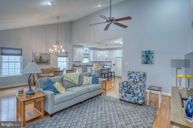 living room with ceiling fan with notable chandelier, light hardwood / wood-style floors, high vaulted ceiling, and sink