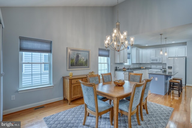 dining area featuring an inviting chandelier, light hardwood / wood-style flooring, lofted ceiling, and sink