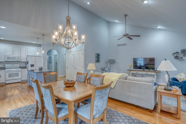 dining room with light wood-type flooring, ceiling fan with notable chandelier, and high vaulted ceiling