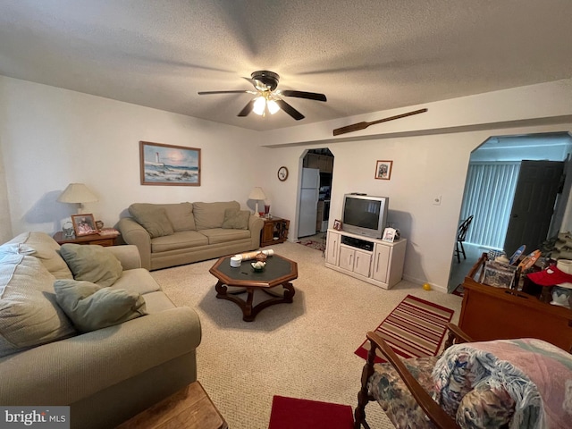 living room featuring arched walkways, light carpet, ceiling fan, a textured ceiling, and baseboards