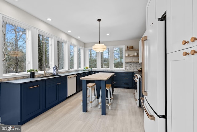 kitchen with blue cabinets, white appliances, a sink, open shelves, and dark countertops