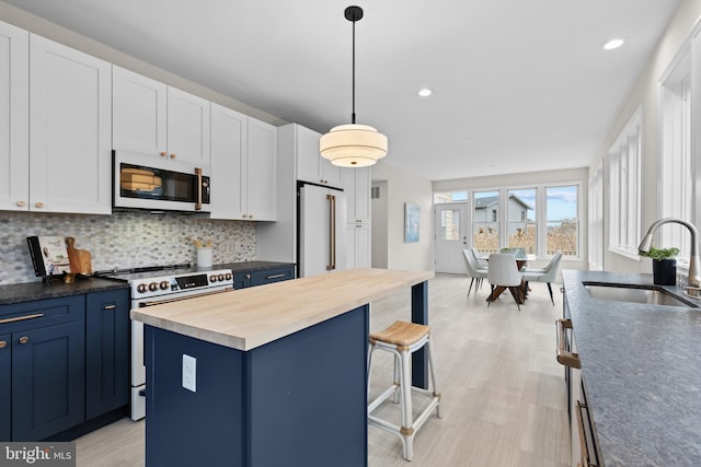 kitchen with white appliances, butcher block countertops, a kitchen island, a sink, and white cabinets