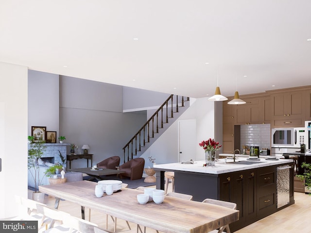 kitchen featuring decorative light fixtures, sink, a kitchen island with sink, oven, and dark brown cabinets