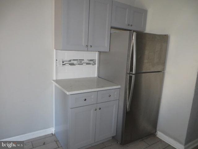 kitchen featuring gray cabinetry, stainless steel fridge, light tile patterned floors, and backsplash