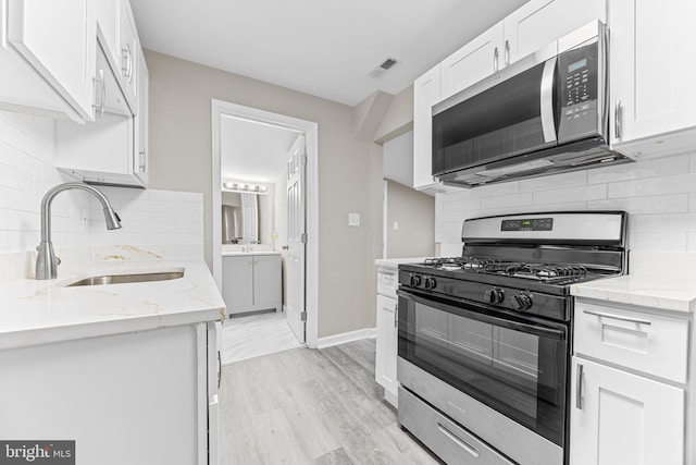 kitchen with sink, stainless steel appliances, white cabinetry, and light hardwood / wood-style flooring