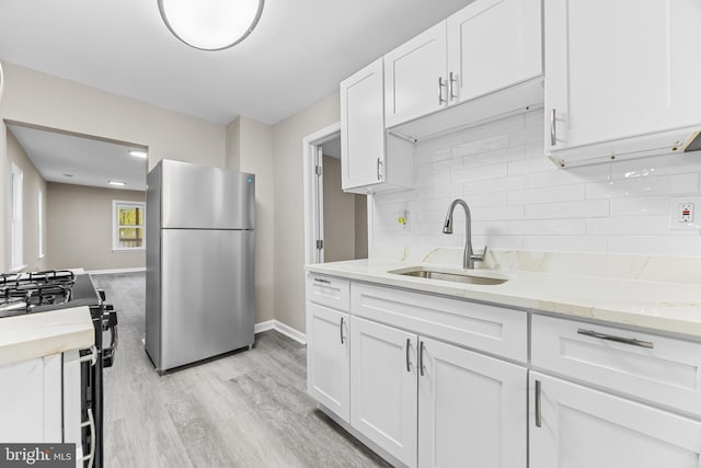 kitchen featuring white cabinets, stainless steel fridge, black gas stove, and sink