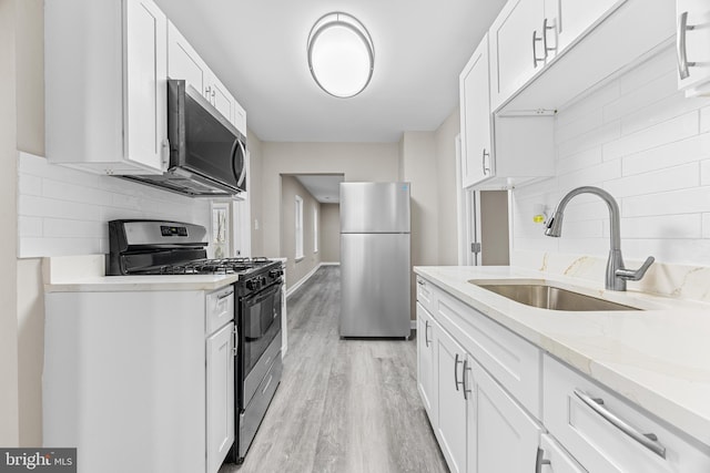 kitchen with light stone countertops, white cabinetry, sink, stainless steel appliances, and light wood-type flooring