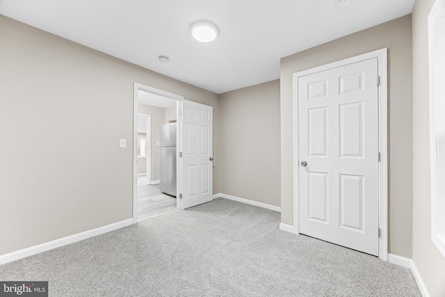 unfurnished bedroom featuring stainless steel fridge and light carpet