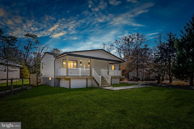 back house at dusk featuring a porch and a lawn