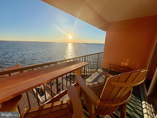 balcony at dusk featuring a water view