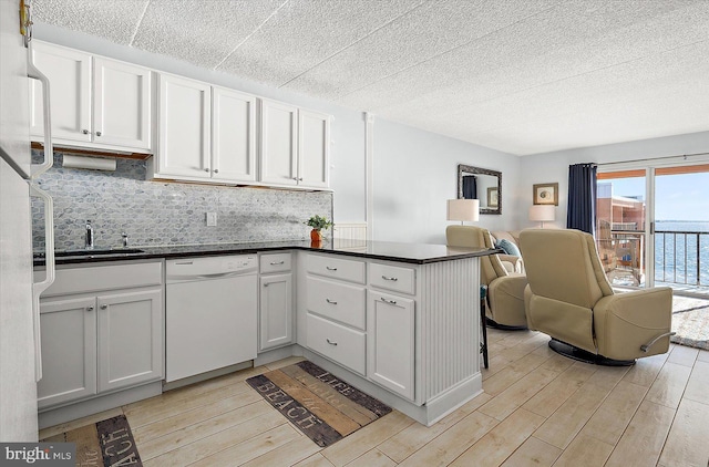 kitchen with kitchen peninsula, backsplash, sink, dishwasher, and white cabinetry