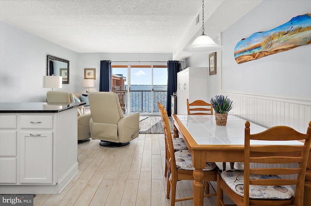 dining area with light hardwood / wood-style flooring, a water view, and a textured ceiling