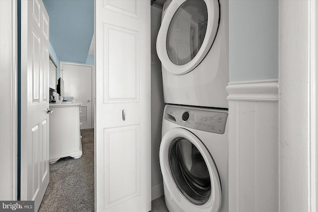 clothes washing area featuring dark colored carpet and stacked washer and clothes dryer