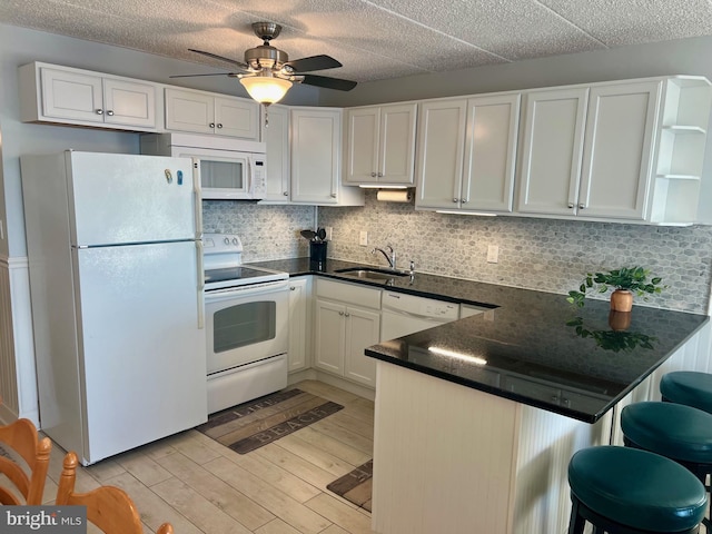 kitchen with kitchen peninsula, a breakfast bar, white appliances, sink, and white cabinets