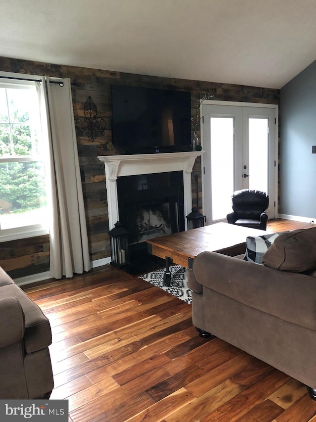 living room featuring hardwood / wood-style floors, a large fireplace, vaulted ceiling, and french doors