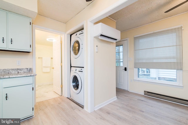 clothes washing area with stacked washer and dryer, light hardwood / wood-style flooring, a textured ceiling, and a baseboard heating unit