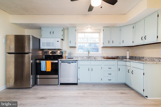 kitchen featuring appliances with stainless steel finishes, a textured ceiling, light hardwood / wood-style floors, and sink