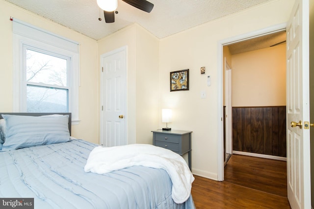 bedroom featuring dark hardwood / wood-style flooring, a textured ceiling, ceiling fan, and wood walls